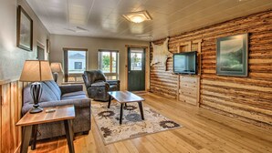 Ein gemütliches Wohnzimmer mit Sofa, Sessel, Couchtisch und einem an einer Holzwand befestigten Fernseher.