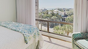 A hotel room with a bed, a chair, and a large window offering a view of the cityscape. - Retreat 514 - 2nd Row, Great View, Pool, Ocean! (Pawleys Island)