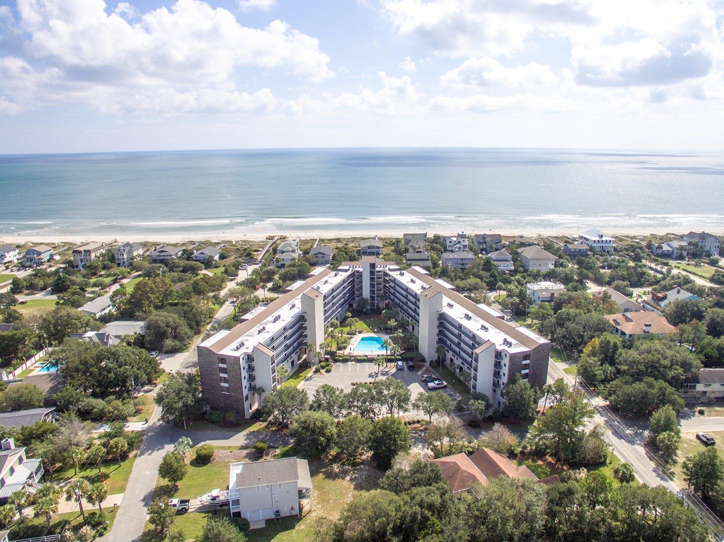 A coastal hotel with a central pool, surrounded by residential buildings and a beach.