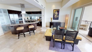 A modern kitchen with dark cabinetry, a central island with stools, and a dining area with a glass table and chairs.
