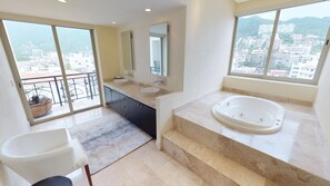 A modern bathroom with a large bathtub, a sink, and a mirror. It has large windows offering a view of the city.