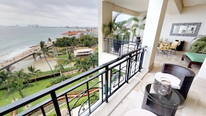 A balcony with a view of the beach and cityscape, furnished with wicker chairs and a glass table. - Luxury Beachfront Condo! 3BD Condo for rent in Los Muertos Beach, Puerto vallart (Puerto Vallarta)