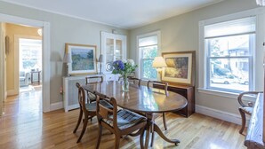 Une salle à manger avec une table en bois, des chaises, un vase de fleurs et des œuvres d’art encadrées accrochées aux murs.