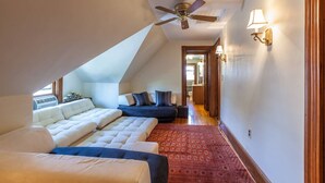 Une chambre avec un plafond en pente, un ventilateur de plafond, un lit, un canapé et un tapis à motifs.