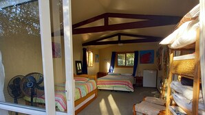 A cozy bedroom with two beds, a fan, and a small kitchenette. - Tui's Rest Whangamata- DOGS WELCOME, suitable for families (Whangamata)