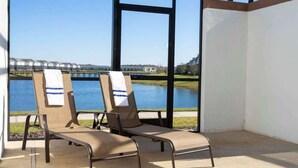 A balcony with two lounge chairs, one with a towel, overlooking a body of water and a distant bridge. - Lake View Private Pool Townhouse at Storey Lake 4861 (kissimmee)