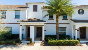 A two-story building with a central entrance, a covered porch, and a palm tree. - Lake View Private Pool Townhouse at Storey Lake 4861 (kissimmee)
