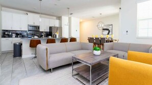 A modern living room with a sectional sofa, a dining area with a table and chairs, and a kitchen with white cabinets and appliances. - Lake View Private Pool Townhouse at Storey Lake 4861 (kissimmee)