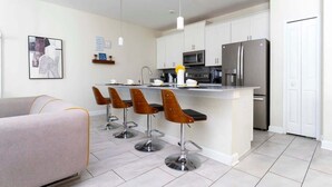 A modern kitchen with a central island, bar stools, a refrigerator, and a microwave. - Lake View Private Pool Townhouse at Storey Lake 4861 (kissimmee)