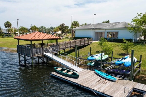 Un muelle con un barco pequeño, una zona de estar cubierta y un edificio de techo rojo.