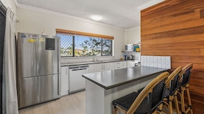 A kitchen with a stainless steel refrigerator, a dishwasher, a window with a view, and a wooden wall.