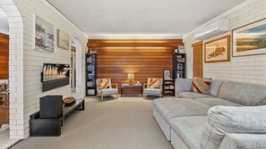A cozy living room with a fireplace, a sofa, armchairs, and a bookshelf.