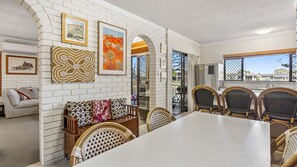 A dining area with a white table, wicker chairs, and a brick wall with artwork.