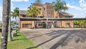 A multi-story building with a covered parking area, brick exterior, and palm trees. - Anjuna, 2 bedroom apartment on canal (Mooloolaba)
