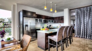 Uma cozinha moderna com ilha central, eletrodomésticos de aço inoxidável e área de jantar com cadeiras de vime.
