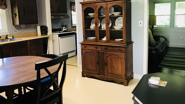 A kitchen with a dining table, chairs, a cabinet with dishes, a stove, and a ceiling fan.