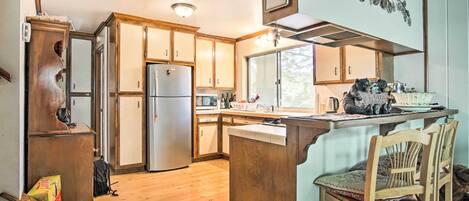 A kitchen with wooden cabinets, a refrigerator, a dining area with a table and chairs, and a window providing natural light.