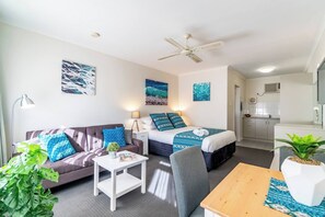 A modern hotel room with a sofa, a bed with patterned bedding, a small table, a chair, and a ceiling fan.