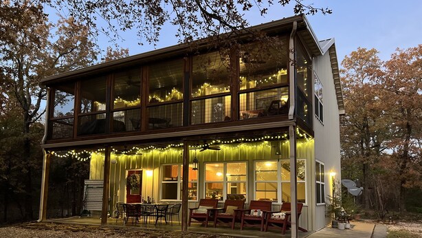 Una casa de dos pisos con un patio cubierto, luces colgantes y mobiliario exterior.