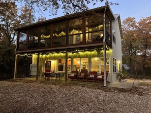 Une maison à deux étages dotée d’un patio couvert, de guirlandes lumineuses et de meubles d’extérieur.