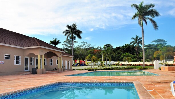 A swimming pool area with a building, palm trees, and a playground. - 2Bedrooms 2Bathroom - Swimming pool - Gated community - Drier - Free Wifi (Ocho Rios)