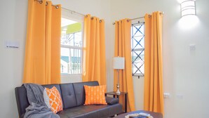 A modern living room with a sofa, a coffee table, and orange curtains. - 2Bedrooms 2Bathroom - Swimming pool - Gated community - Drier - Free Wifi (Ocho Rios)