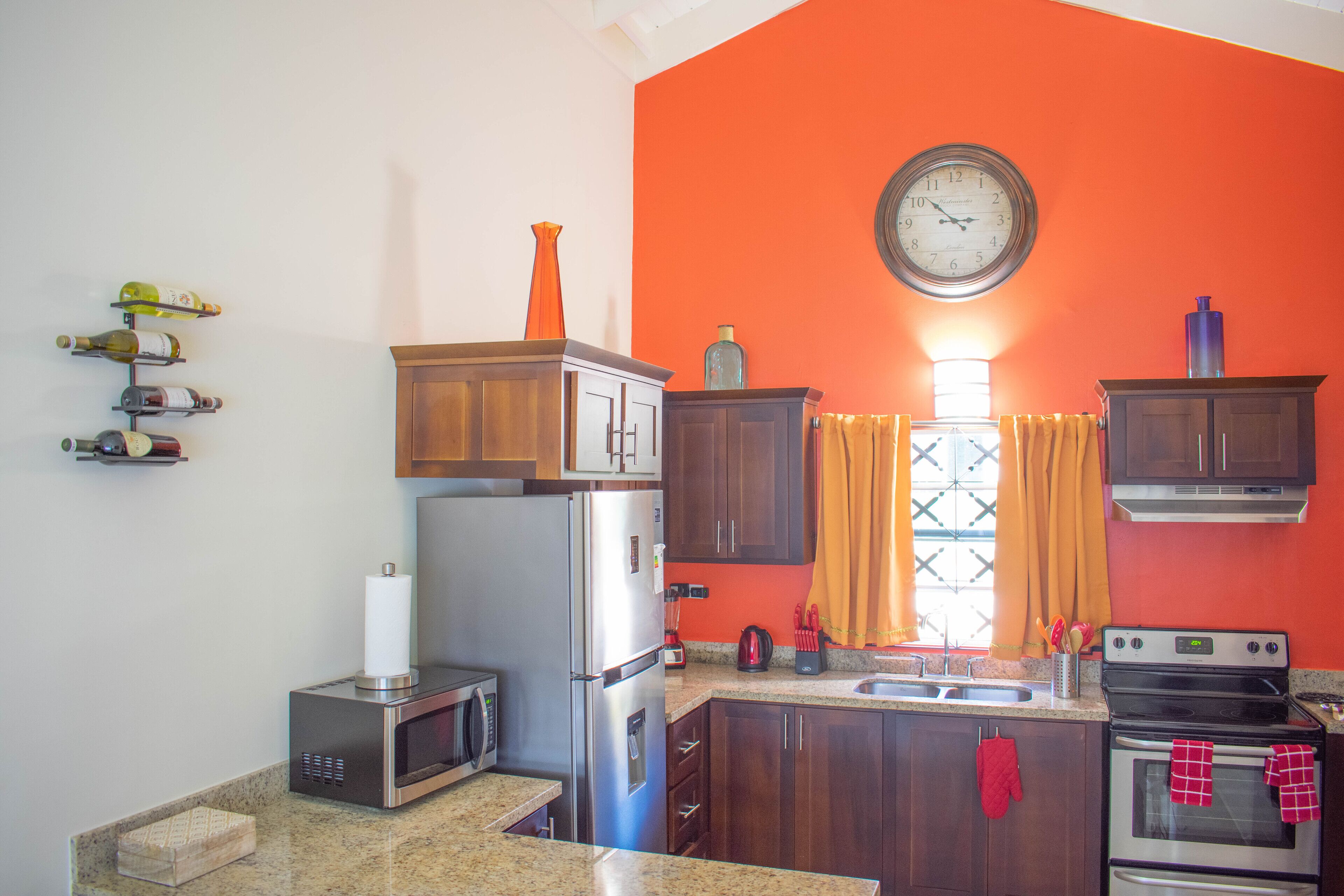 A kitchen with a refrigerator, microwave, stove, and a clock on the wall.