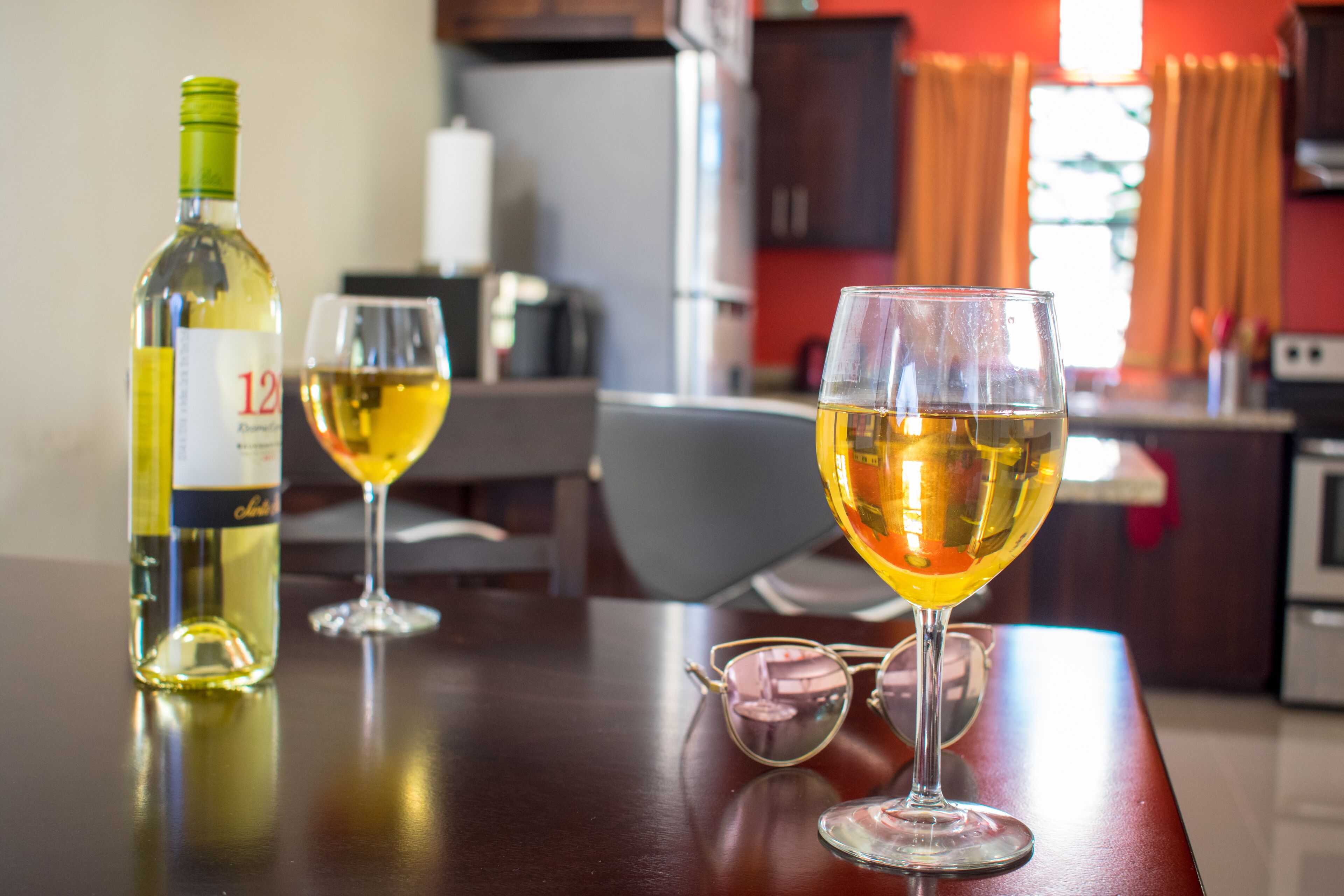 A bottle of wine and two wine glasses on a wooden table in a kitchen.