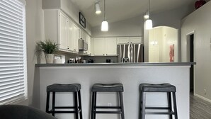 A modern kitchen with white cabinets, a central island with stools, and pendant lighting.
