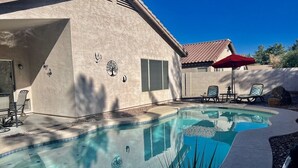 A swimming pool with a tiled edge, surrounded by a patio area with chairs and a red umbrella.
