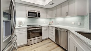 Een moderne keuken met roestvrijstalen apparatuur, witte kasten en een betegelde achterwand.