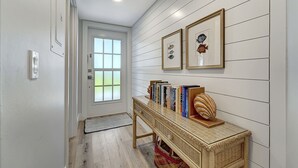 Een gang met een houten bankje, een viskunstwerk en een deur naar een kamer.