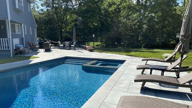 En swimmingpool med ett inbyggt bubbelbad, omgiven av solstolar och en terrass.