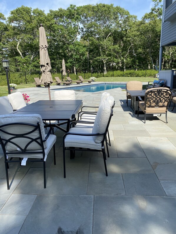 Une terrasse extérieure avec une piscine, des chaises longues et une table avec des chaises.