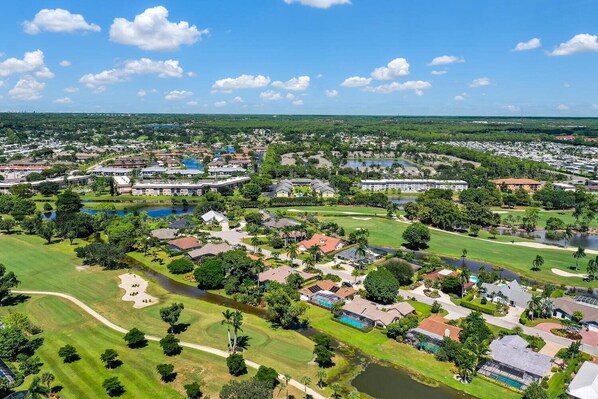 A golf course with residential buildings, a large body of water, and a clear sky. - TORREY PINES - Single Family Pool Home in Lely Country Club (Naples)