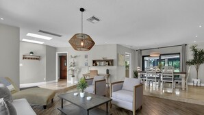 A spacious living room with a modern design, featuring a large coffee table, comfortable seating, and a dining area with a view. - TORREY PINES - Single Family Pool Home in Lely Country Club (Naples)