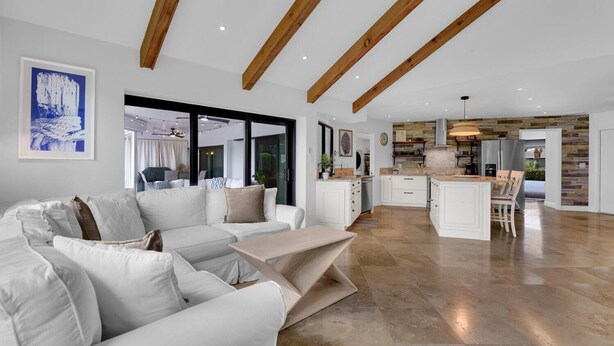 A spacious living area with a modern white sofa, a coffee bar, and a kitchen with wooden beams. - TORREY PINES - Single Family Pool Home in Lely Country Club (Naples)