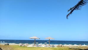 A beach with two wooden umbrellas and lounge chairs, a clear blue sky, and the ocean in the background. - Oceanview Sealofts: NO spiral staircase & only 25 steps to ocean (Frigate Bay)