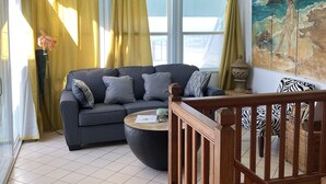 A living room with a sofa, a coffee table, and a painting on the wall. - Oceanview Sealofts: NO spiral staircase & only 25 steps to ocean (Frigate Bay)