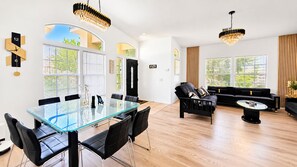 A modern living space with a glass-top dining table, black leather chairs, a black sofa, and a coffee table. - The Panorama Oasis: Saltwater Pool, Spa & EV Charger (Cathedral City)