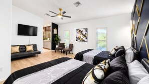 A modern hotel room with two beds, a flat-screen TV, a ceiling fan, a seating area with a sofa and chairs, and artwork on the walls. - The Panorama Oasis: Saltwater Pool, Spa & EV Charger (Cathedral City)