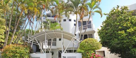 A modern building with a curved entrance, surrounded by palm trees and a well-maintained garden.