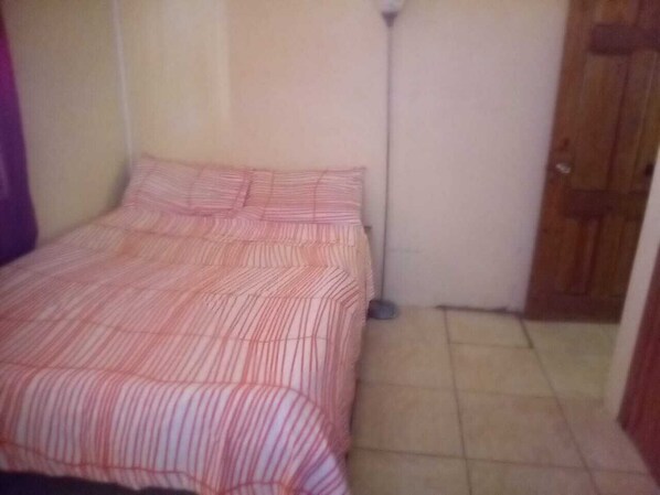Une petite chambre avec un lit simple, une couvre-lit à rayures, une lampe sur pied et une porte en bois.