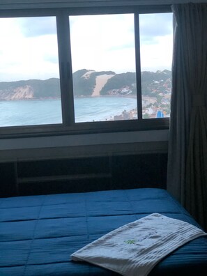 Une chambre avec un lit, une fenêtre donnant sur une plage et des collines, et un rideau à la fenêtre.