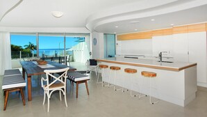 Una cucina moderna con angolo bar, ampie finestre vista oceano e zona pranzo panoramica.
