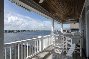 Una terraza de madera con barandas blancas que da a un cuerpo de agua, con varias sillas Adirondack blancas y una mesa.