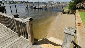 Une jetée en bois mène à une plage de sable, d’où l’on a une vue dégagée sur l’eau et les bâtiments situés au loin.
