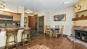 A kitchen with wooden bar stools, a dining table with chairs, a fireplace, and a tiled backsplash. - Entire 1BR apt, Sleeps 4, Wi-Fi, Close to Slopes (Vail)