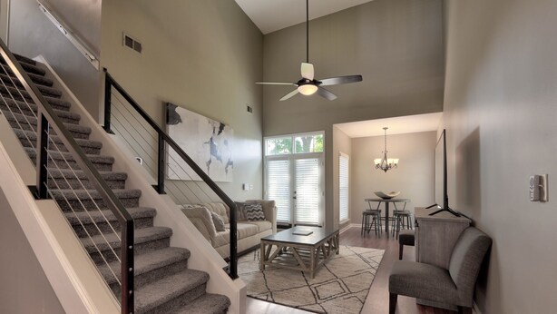 Un vaste espace de vie comprenant un escalier, un ventilateur de plafond et un coin repas avec une table et des chaises.
