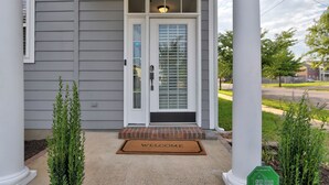 Une maison à l’extérieur grise, avec une porte d’entrée blanche dotée d’un panneau en verre, un paillasson et un tapis d’entrée.